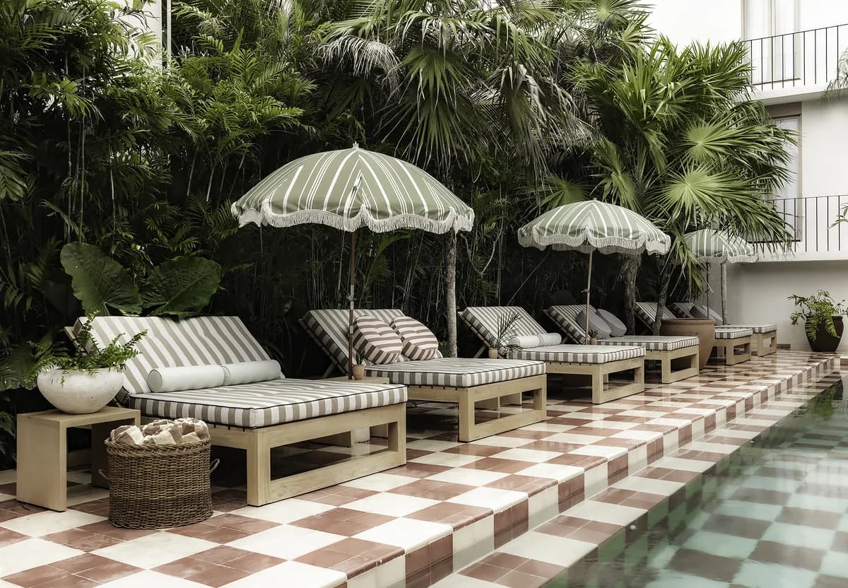 Alberca de Hotel Panamera: azulejo damero en terracota, camastros a rayas y sombrillas entre vegetación